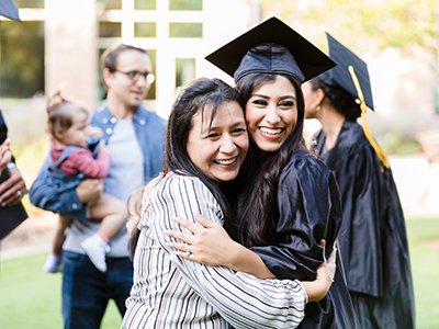 Mother and graduating daughter pose cheek to cheek for photo Hands holding